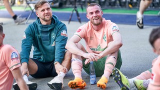 Die Werder-Stürmer Niclas Füllkrug und Marvin Ducksch hocken mit ihren Mitspielern nach dem Sieg vor der Werder-Fankurve in Berlin.