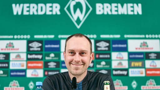 Werder-Trainer Ole Werner schmunzelt verschmitzt während einer Pressekonferenz.