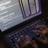 Quellcode eines Webservers sowie die Windows-Eingabeaufforderung sind einem Laptop im Dunkeln zu sehen. Hände tippen auf der Tatstatur des Laptops.