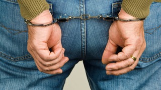 Die Hände einer Person sind hinter dem Rücken mit Handschellen gefesslet