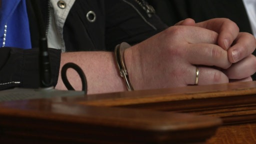 Zu sehen sind die Hände des Angeklagten, welche in Handschellen gelegt sind.