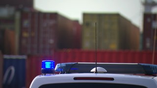 Im Vordergrund sieht man das Blaulicht eines Polizeiwagens und im Hintergrund sind große Container zu sehen.