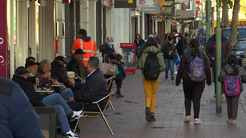 Menschen sitzen und laufen in einer Straße.