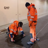 Bauarbeiter stehen in einem leeren Tunnel und arbeiten am Boden.