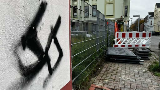 An einer Hauswand an einer Straße ist ein gesprühtes Hakenkreuz zu sehen.
