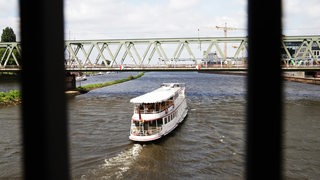 Ein kleines Schiff fährt unter einer Brücke durch