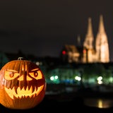 Ein Halloween-Kürbis liegt bei Dunkelheit auf einer Mauer. Im Hintergrund sieht man eine Kathedrale.