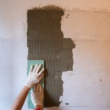 Eine Person drückt Fliesen auf eine mit Spachtelmasse versehene Wand.