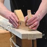 Ein Hobel fährt über ein Holzbrett. Späne fliegen.