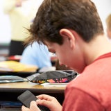 Ein Schüler tippt heimlich während des Unterrichts eine Nachricht auf sein Mobiltelefon.