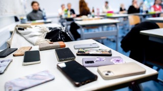 Zahlreiche Smartphones liegen in der Schule auf einem Tisch, die die Schüler abgeben mussten.