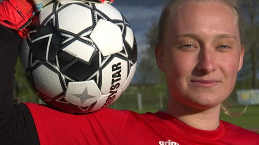 Die Fußballspielerin Hanna Engel hält einen Fußball auf ihrer Schulter. 