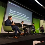 Mehrere Personen sitzen auf einem Podium und unterhalten sich.