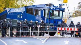 Einsatzkräfte der Polizei stehen vor einem Wasserwerfer vor dem Stadion. Die Polizei begleitet das als Hochrisikospiel eingestufte Derby mit einem Großaufgebot.
