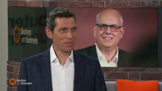 Der Reporter Hauke Hirsinger im Studio von buten un binnen, im Huntergrund ein Bild von Andreas Bovenschulte.