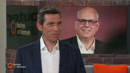 Der Reporter Hauke Hirsinger im Studio von buten un binnen, im Huntergrund ein Bild von Andreas Bovenschulte.