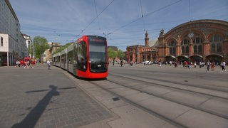 Eine Straßenbahn fährt die Haltestelle Hauptbahnhof Bremen an. Im Hintergrund ist der Hauptbahnhof Bremen und viele Passanten zu sehen.