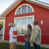 Mann, Frau und eine Maklerin stehen vor einem Haus und betrachten das Objekt