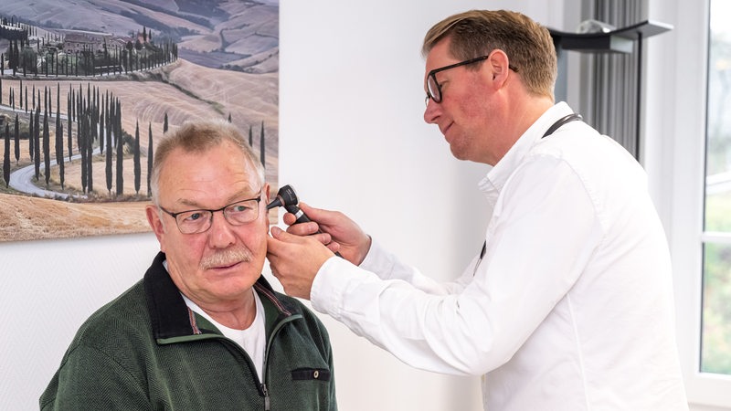 EIn Hausarzt untersucht mit Hilfe eines Otoskops das Ohr eines Patienten