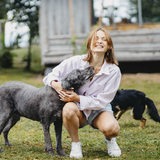 Eine junge Frau spielt mit ihren Hunden vor einer Hütte.
