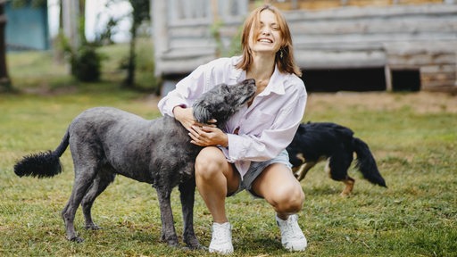 Eine junge Frau spielt mit ihren Hunden vor einer Hütte.