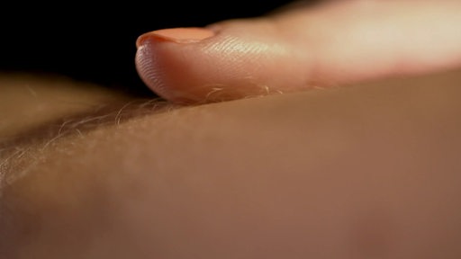 Eine Nahaufnahme von einem Finger der über eine leicht behaarte Hautstelle fährt. 