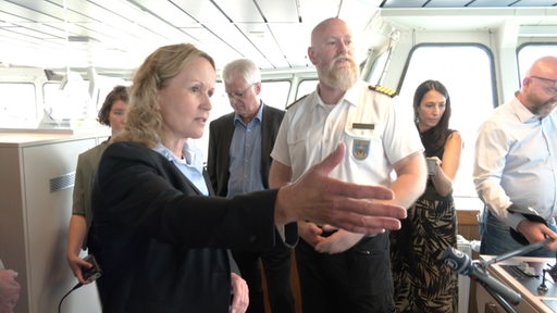 Die Umweltministerin Lehmke steht mit dem Kapitän in der Kommandobrücke eines Schiffes.