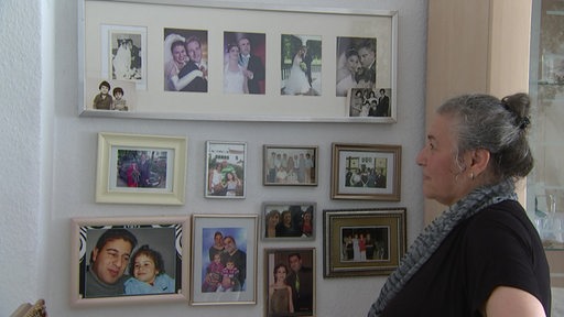 Türkische Frau betrachtet Wand mit gerahmten Familienfotos.