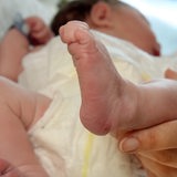 In einer Geburtsklinik hält eine das Füßchen eines wenige Stunden alten Neugeborenes in ihren Händen.