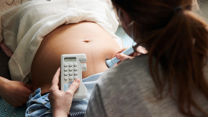Eine Hebamme hört mit einem Ultraschallgerät die Herztöne eines ungeborenen Kindes ab. Die Frau ist im 2. Trimester schwanger und liegt auf einem Bett in der Hebammenpraxis. In Bremen fehlten Hebammen vor allem in ärmeren Statteilen. 