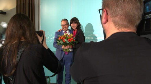 Der neue Landesvorsitzende der CDU, Heiko Strohmann, steht neben einer Frau und hält einen Blumenstrauß in der Hand.