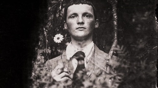 Der Künstler Heinrich Vogeler mit einer Blume in der Hand.