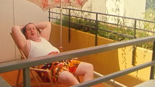 Ein Urlauber auf seinem Balkon in einer lässigen Pose.