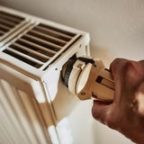 Eine Hand an einem Heizkörper-Thermostat