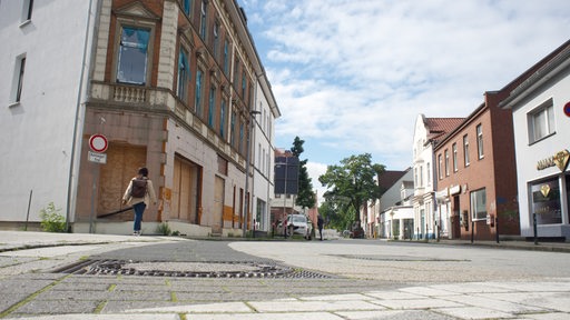 Öde Einkaufsstraße mit marodem Eckhaus und einsamer Passantin im Vordergrund