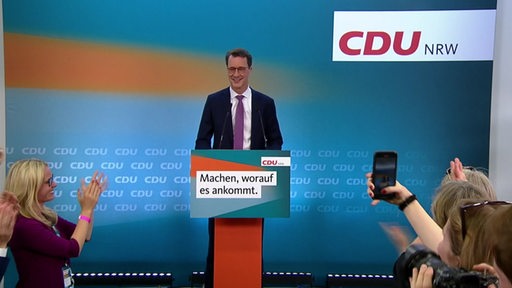 Der CDU-Politiker Hendrik Wüst wird nach einer gewonnenen Wahl auf dem Podium gefeiert.