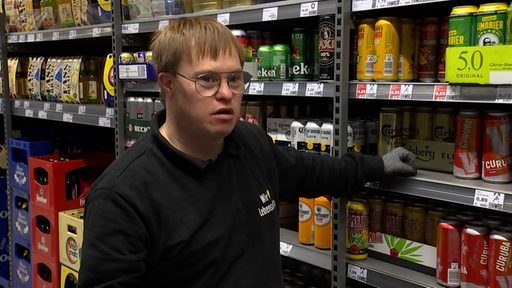 Ein Mitarbeiter eines Supermarktes, Henning Wolters, steht vor einem gefüllten Getränkeregal.