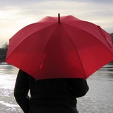 Bei trübem Herbstwetter und Regen schaut eine junge Frau mit rotem Regenschirm über die Weser bei Bremen.