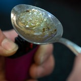 Über der Flamme eines Feuerzeuges kocht eine drogensüchtige Person Heroin in einem Löffel auf.