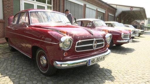 Es sind mehrere nebeneinander stehende Oldtimer zu sehen. Im Vordergrund steht ein roter Borgward.