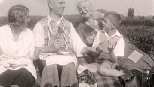Eine lachende Familie sitzt auf einer Wiese.