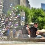 Menschen sitzen an einem Brunnen, die Sonne scheint