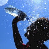 Bei strahlend blauem Himmel und tropischen Temperaturen schüttet sich ein Junge Wasser aus einer Flasche über seinen Kopf.