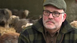 Der Hobbyschäfer Ralf Reinhardt- Im Htergrund befinden sich Schafe.