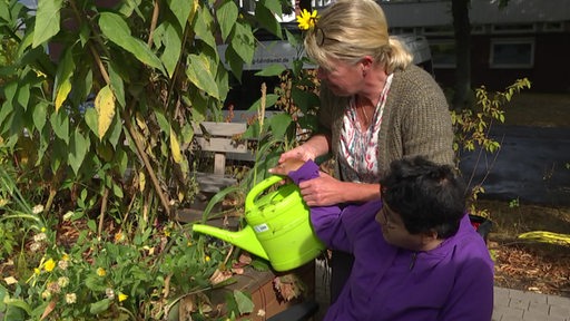 Friedehorstbewohnerin und Betreuerin gießen die Pflanzen im Hochbeet.