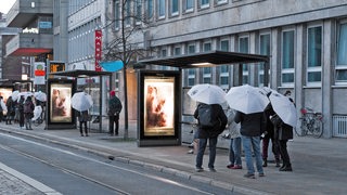 Menschen mit weißen Regenschirmen an einer Bushaltestelle in der Bremer Innenstadt