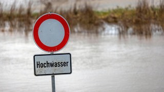 Ein Schild warnt vor Hochwasser. Im Hintergrund Wasser.