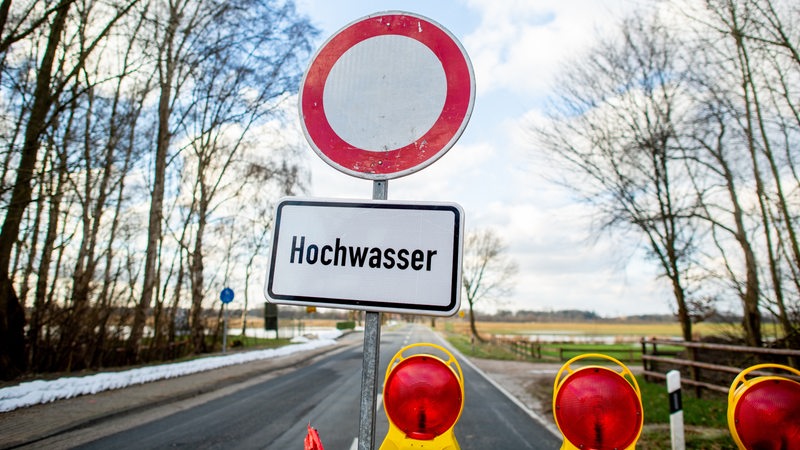 Eine Absperrbake und ein Schild mit der Aufschrift "Hochwasser" steht vor einer gesperrten Straße.