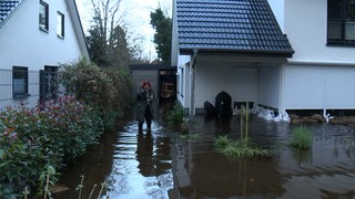 Eine Frau steht vor ihrem überfluteten Haus in Lilienthal.