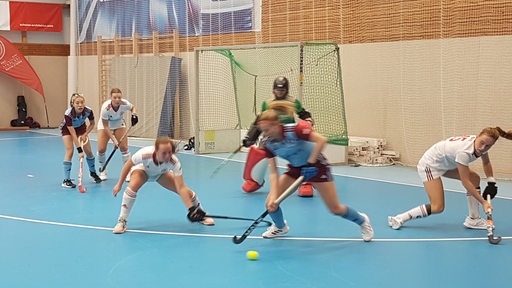 Hockey-Spielerinnen des Bremer HC und des Uhlenhorster HC kämpfen in der Halle vor dem Tor der Bremerinnen um den Ball.